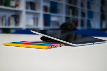 Tablet  with a blank screen and colorful crayons on the desk table in the library