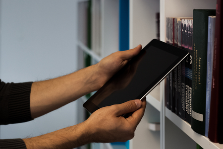 Guy or man or student or businessman show a tablet with a blank screen near bookshelf in the library with his handsの写真素材