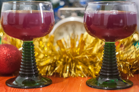 Christmas and New Year celebration holiday clock with two glasses of red wine and red ball covered with yellow fir on the red tableの写真素材