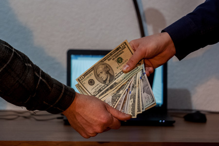 Two guys or businessmen giving dollars to each other. Laptop in the backgroundの写真素材