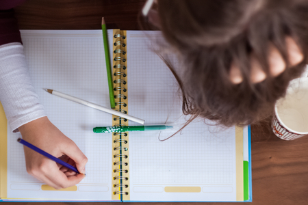 Beautiful cute little blond girl with glasses and purple dress working or drawing or coloring in the...