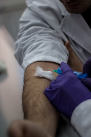 Doctor and patient sitting across from each other, while the doctor prepares a needle to pull out the blood of the patient to findの写真素材