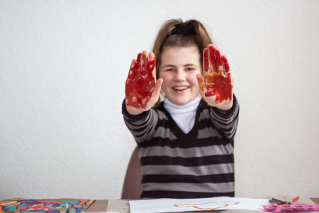 Girl painting with brush and colorful paint and smeared hands of colorsの写真素材