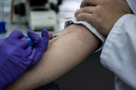 Doctor and patient sitting across from each other, while the doctor prepares a needle to pull out the blood of the patient to findの写真素材