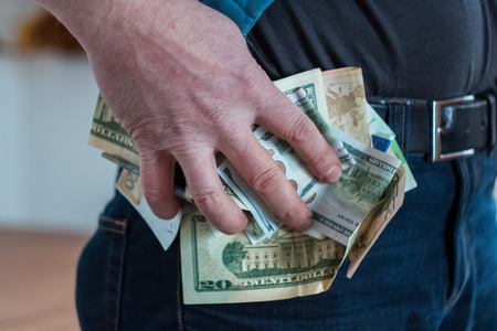 Paper money man holding tightly pinched in his hand, trying to slip into your pocketの写真素材