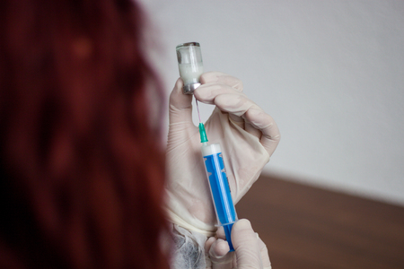 Young doctor prepares an injection to a patient, the injected liquid in the needle, holding very carefullyの写真素材