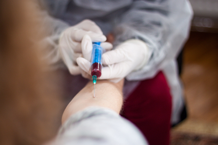 Doctor and patient sitting across from each other, while the doctor prepares a needle to pull out the blood of the patient to findの写真素材