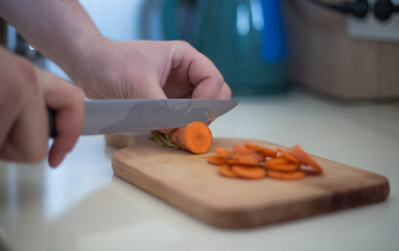 Chef is cutting carrot on a wooden cutting board with sharp knifeの写真素材