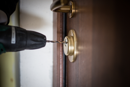 Crime, robbery, masked thief, burglar, trying to break into a flat, a drill in the hands, a cap on the head, and a gloves on the hands that there are no fingerprints as evidenceの写真素材