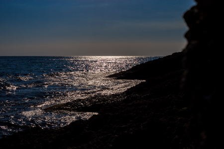 Heavenly beautiful coast in the dawn or evening peaceful coastline with blue sea shining and blue sky in the horizon and rocks in the shadow during summerの写真素材