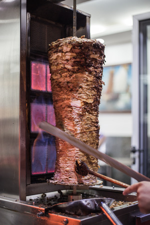 Traditional turkish doner kebap being prepared on the street. Chicken and beef doner kebap with fire on the side cooked and sliced with knifeの写真素材