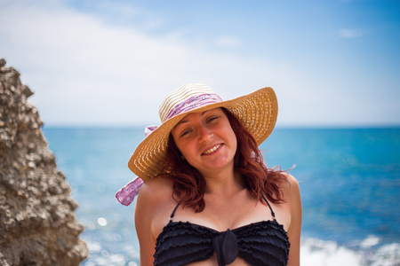 A young girl on the beach, enjoying a holiday in the sun by the sea, a hat on the head, in the background blue seaの写真素材
