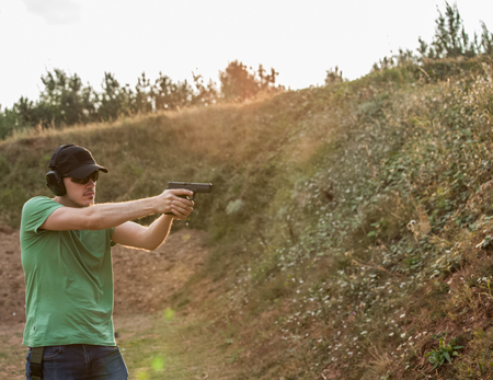 Handsome and muscular caucasian handsome guy firing furiously from fire gun glock pistol violent hard training in the nature for professional army special forces aiming and shooting the enemy targetの写真素材