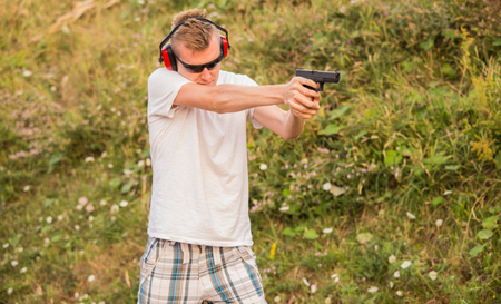 Young and strong caucasian blond guy firing bullets at the enemy target in the wilderness. Aiming to...