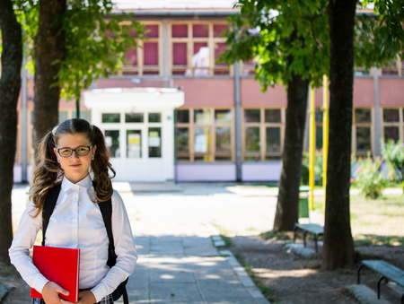Young blue-haired girl with a backpack standing in front of school, beginning of school year, uniform, backpack, books, school, yardの写真素材