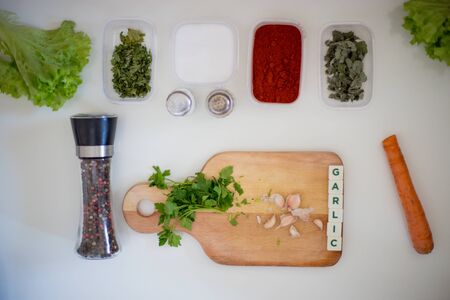 Preparing for lunch to eat on a white kitchen table with wooden cutting board, red pepper, green parsley, colorful pepper.Green salad and word garlicの写真素材
