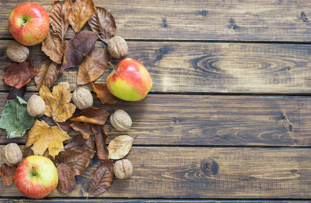 Dry autumn leaves, apples and nuts make a left border on wooden backgroundの写真素材