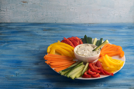 Colorful vegetable sticks in a plate with dip sauce on blue tableの写真素材
