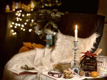 Comfortable place in decrated room for Christmas with chair, plaid, knitting, coffee and sweets. Toning.の写真素材