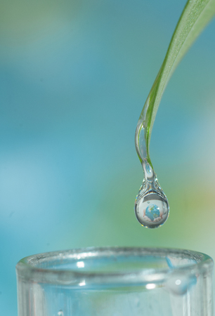 Close up of water drop falling down from the green leaf with earth sphere reflectionの写真素材