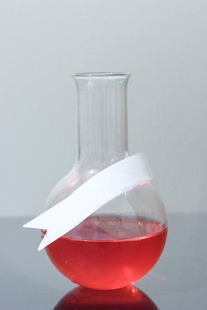 Laboratory flask on grey background with red liquid reactiveの写真素材