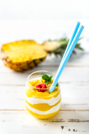 Vertical shot of mango and pineapple smoothie with yogurt in one glass on white tableの写真素材