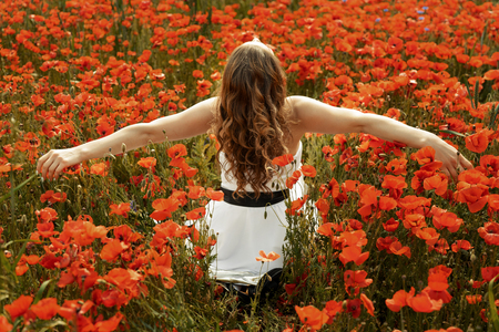 Happy young red-haired woman in poppy field with flying hair and hands lifted upの写真素材