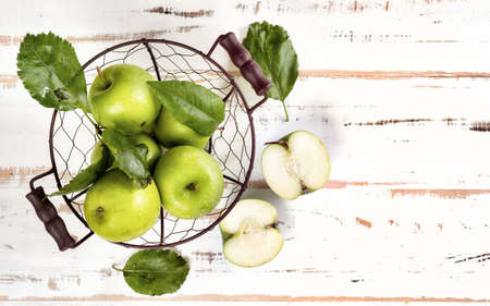 Top view of green apples in wicker basket on white wooden background. Copy spaceの写真素材