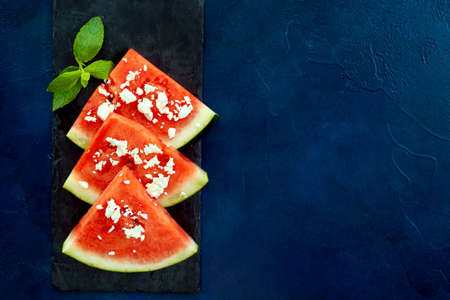 Top view of watermelon slices with feta cheese on blue background. Copy space