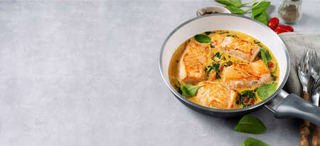 Salmon steaks in a frying pan with cream on light background. Long banner. Copy space