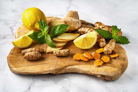 Close up of wooden board with ginger, turmeric, lemons and mint on white background - ingredients...