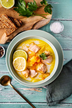 Top view of delicious and healthy salmon soup with plant-based cream, carrots and potato in green plate on rustic turquoise backgroundの写真素材