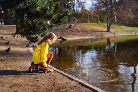 Happy child girl in bright yellow sweater paying with water outdoorsの写真素材
