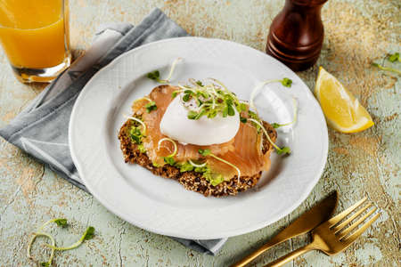 Top view of home-made toast with mashed avocado, salmon, poached egg and microgreens in a plate....