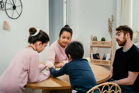 Mixed race family thinking, concentrating and sitting together at the table, while playing with board game. Real life, diversity, digital detox and unplugging from technologyの写真素材