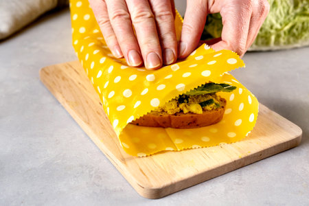 Woman hands wrapping a healthy sandwich in beeswax food wrap and cotton bagの写真素材