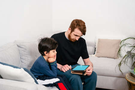 Father and son sitting on sofa with digital tabletの写真素材