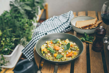 A plate with tasty italian soup minestrone on wooden table outddors in the gardenの写真素材