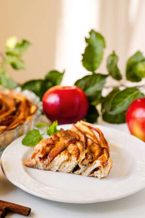 Slice of delicious apple cake on kitchen table with apples and leaves on backgroundの写真素材