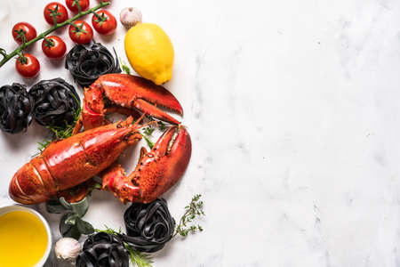 Red delicious freshly cooked lobster with black pasta and vegetables on white background. Top view....
