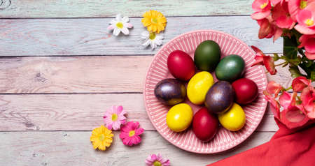 Colorful panted Easter eggs on pink plate and pastel color background with flowers. Easter spring holidaysの写真素材