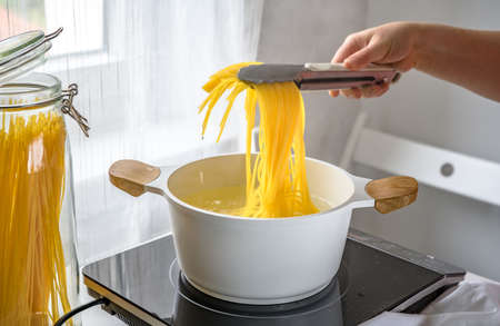 Woman cooking gluten free pasta in white pot at the kitchen. Healthy keto diat conceptの写真素材