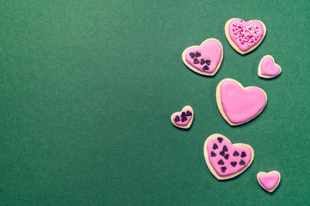 Pnik sugar cookies of heart shape on emerald green background. Trendy flat lay with copy spaceの写真素材