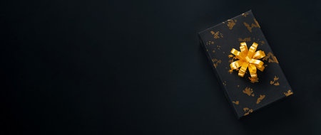 Black present with golden bow on dark background. Black friday or Christmas holidays concept with...