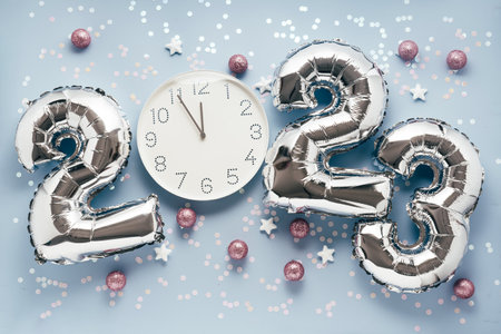 Shiny silber air balloon numbers and white watch at 12 oclock on light blue background with confetti...