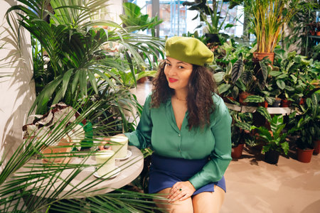 Stylish hipster woman drinking macha tea in green cafe. Trendy biophilic interior design with many green plants. Urban jungleの写真素材
