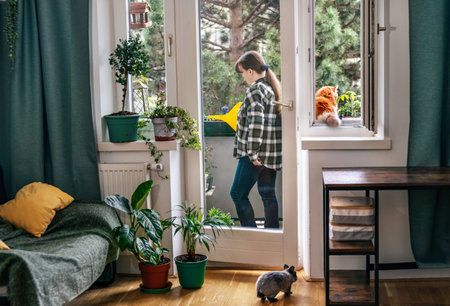 Smiling woman watering flowers on balcony. Cute pets cat and rabbit in her flat. Urban hobby garden, mental health, comfort zone conceptsの写真素材