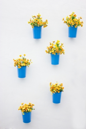 Plastic yellow flowers with metal blue vase hang in row on the wall の写真素材