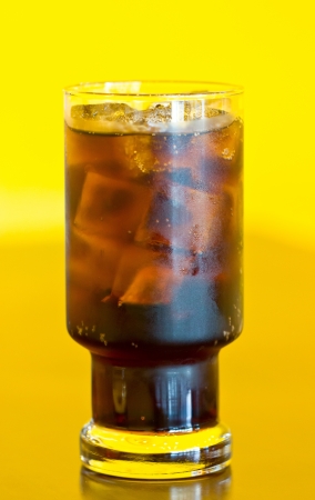 Glass of cola with ice isolated on yellow background の写真素材