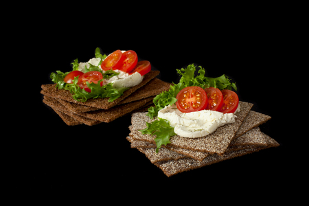 Healthy snack from wholegrain rye crispbread cracker with Cherry tomatoes, salad and soft cheese on black backgroundの写真素材